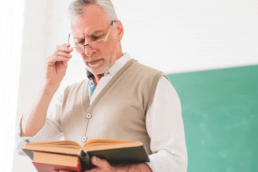 senior-male-professor-reading-book-while-correcting-glasses
