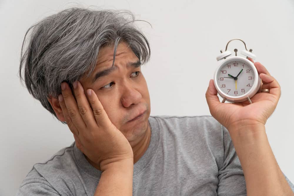 asian-middle-aged-man-is-holding-white-alarm-clock-his-face-showed-boredom-feeling-bad