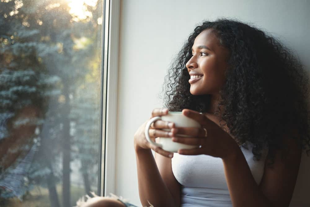 morning-routine-portrait-happy-charming-young-mixed-race-female-with-wavy-hair-enjoying-summer-view-through-window-drinking-good-coffee-sitting-windowsill-smiling-beautiful-daydreamer