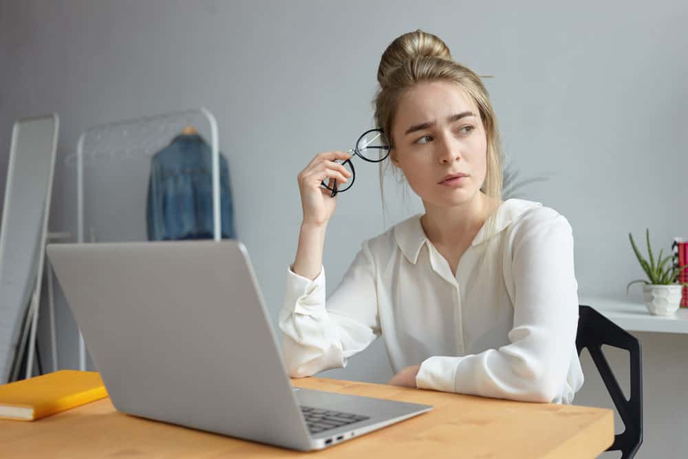 frustrated-exhausted-young-woman-blogger-dressed-white-blouse-holding-round-eyeglasses-looking-away-with-worried-expression-searching-inspiration-trying-write-article-her-blog
