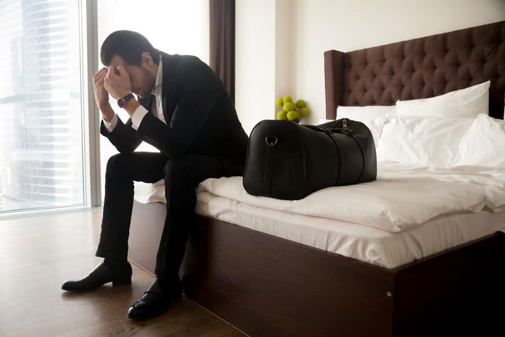 frustrated-man-suit-sitting-bed-besides-luggage-bag