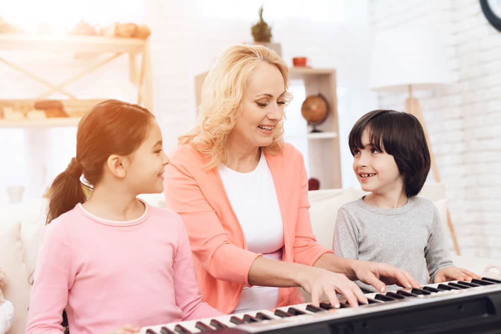 nonna con bambini che insegnano a suonare il pianoforte a casa