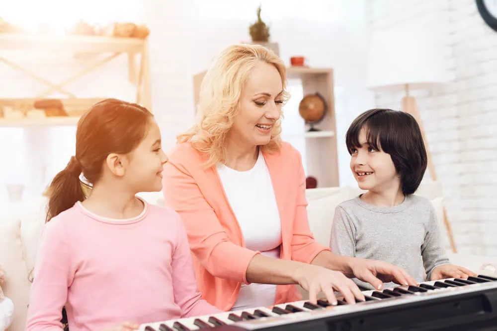 isoäiti-lasten-kanssa-opettaa-soittamaan-pianoa-kotona isoäiti-lasten-kanssa-opettaa-soittamaan-pianoa-kotona