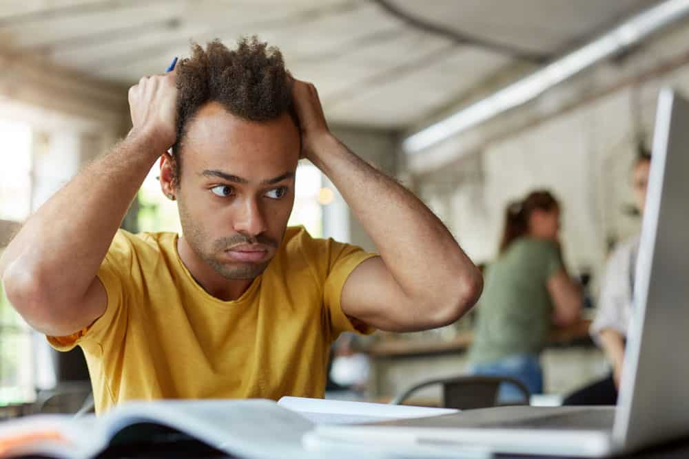 student-feeling-frustrated-sitting-coworking-space-front-open-laptop-computer-holding-head-with-hands-